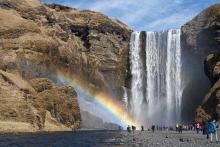 A group of people standing at a waterfall with a rainbow over them.